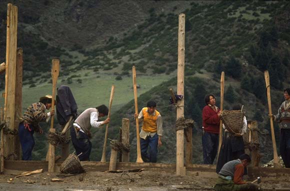 Workers build a wall of the Palpung Buddhism College, which is being constructed on the hill above Palpung. They compact the clay wall by dancing on top of the mix of clay and gravel.