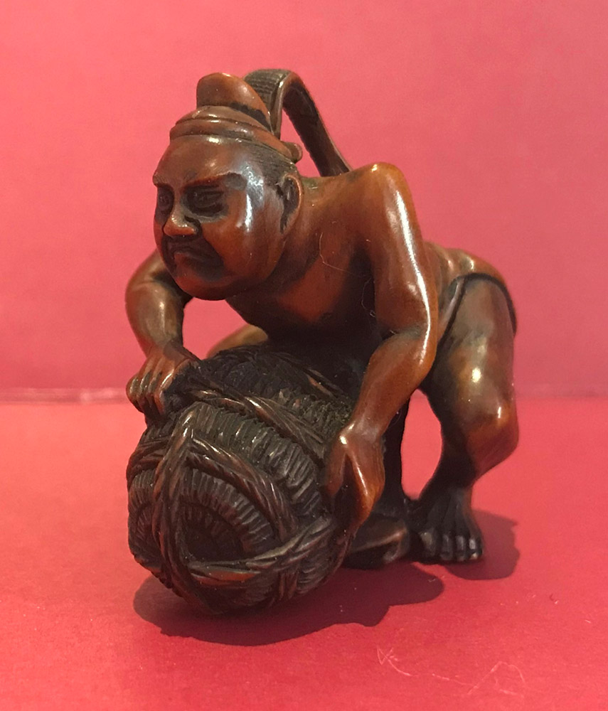 Boxwood netsuke of a man wearing a court hat lifting a rice bale